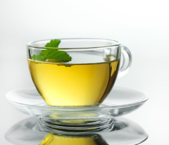 A clear glass cup filled with Green Tea and a mint leaf on a white background